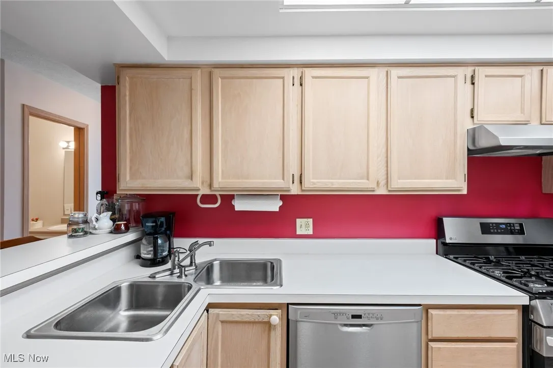 Kitchen with light brown cabinetry, appliances with stainless steel finishes, light countertops, and exhaust hood