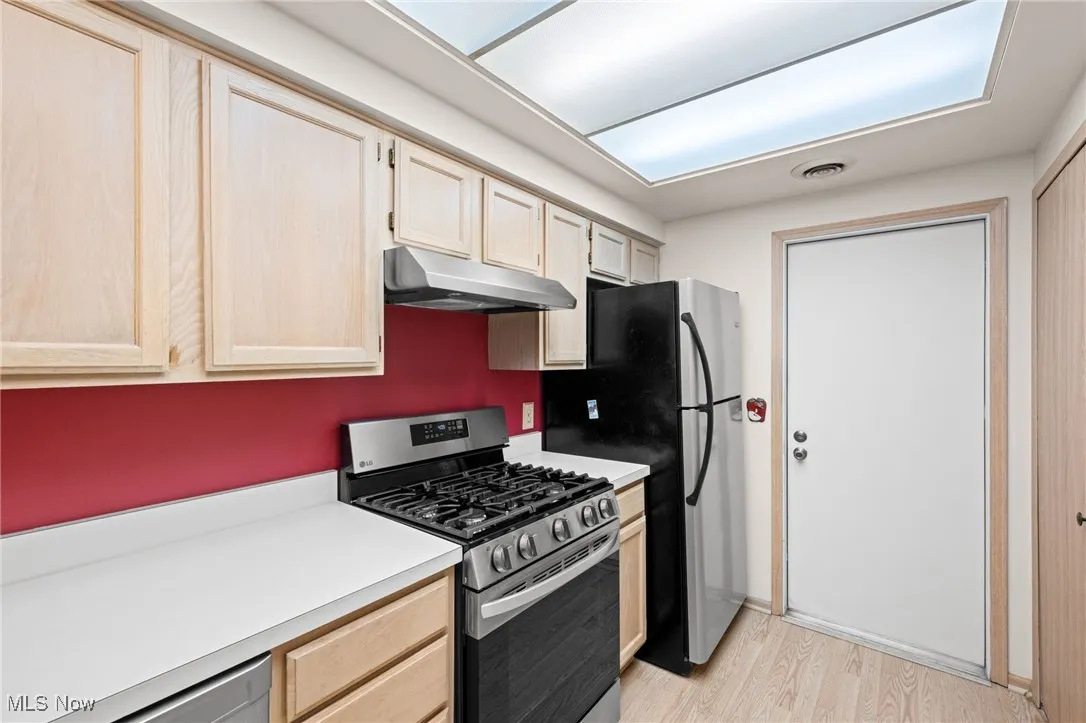 Kitchen with light brown cabinets, gas range, light countertops, light wood-type flooring, and under cabinet range hood