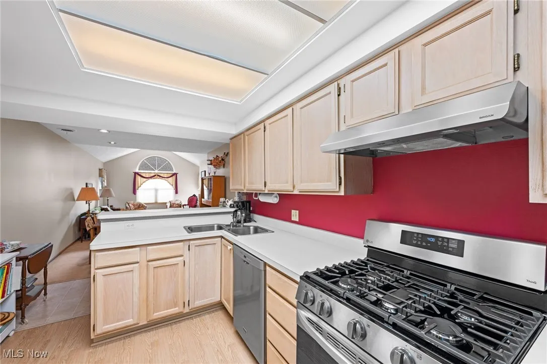 Kitchen with light brown cabinets, stainless steel appliances, open floor plan, and under cabinet range hood