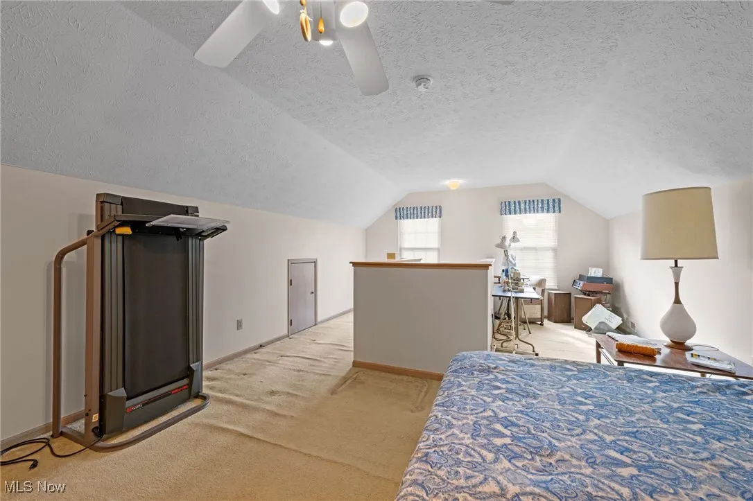 Carpeted bedroom featuring a textured ceiling, vaulted ceiling, and a ceiling fan