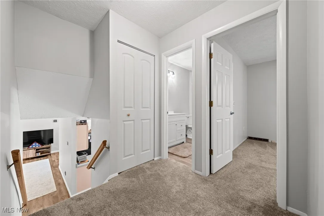 Hallway featuring an upstairs landing, light colored carpet, and a textured ceiling