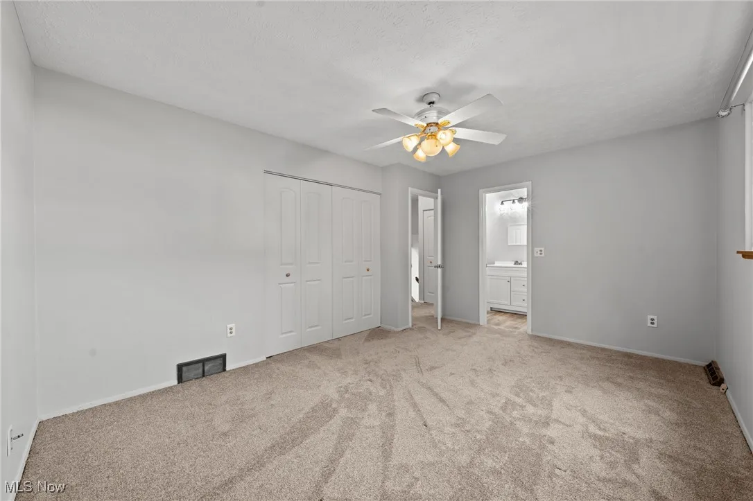 Unfurnished bedroom with light colored carpet, a closet, a ceiling fan, a textured ceiling, and ensuite bath