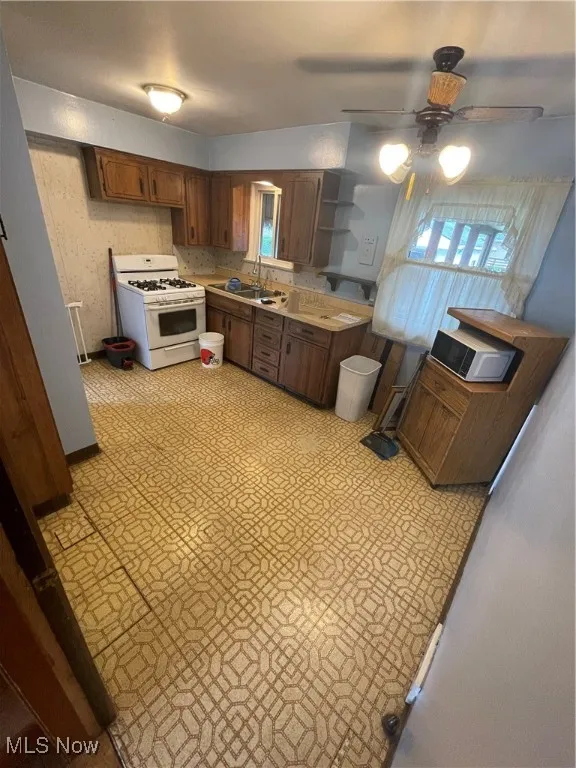 Kitchen featuring white stove, light countertops, open shelves, light flooring, and ceiling fan