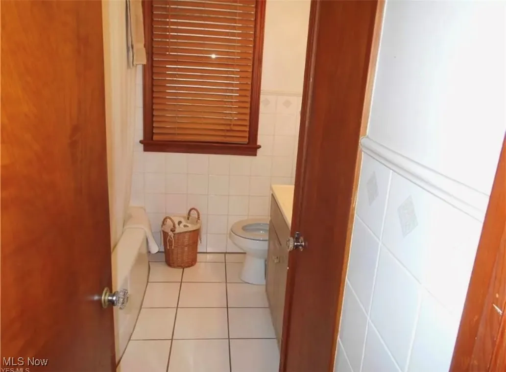 Full bath featuring light tile patterned floors, vanity, shower / bath combo with shower curtain, tile walls, and wainscoting