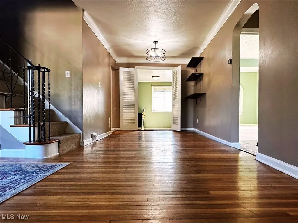 Foyer entrance with dark wood-type flooring, ornamental molding, stairway, a chandelier, and a textured ceiling