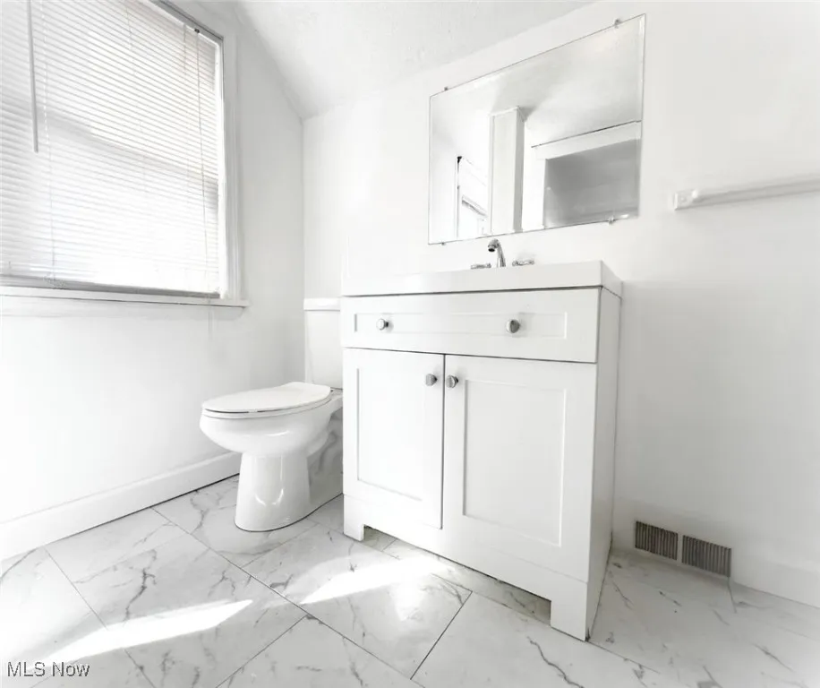 Bathroom with vanity, light marble finish flooring, lofted ceiling, and a textured ceiling