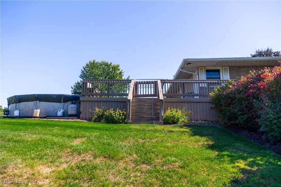 View of grassy yard featuring a wooden deck and stairs
