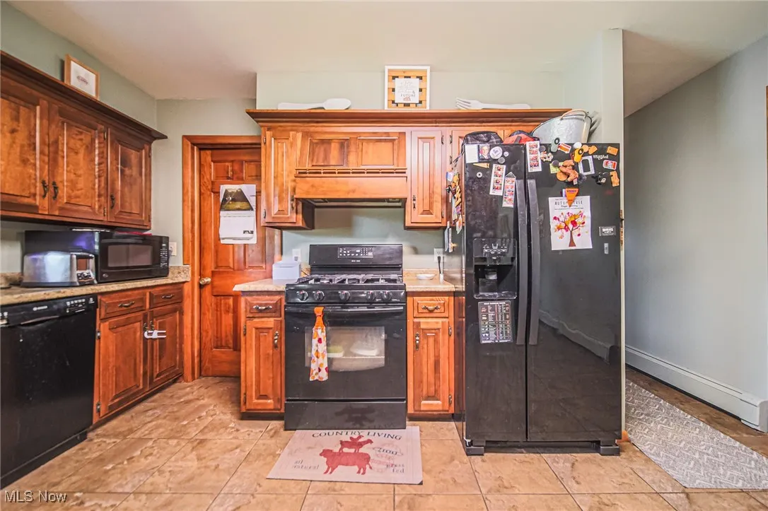 Kitchen featuring black appliances, light tile patterned floors, and brown cabinetry