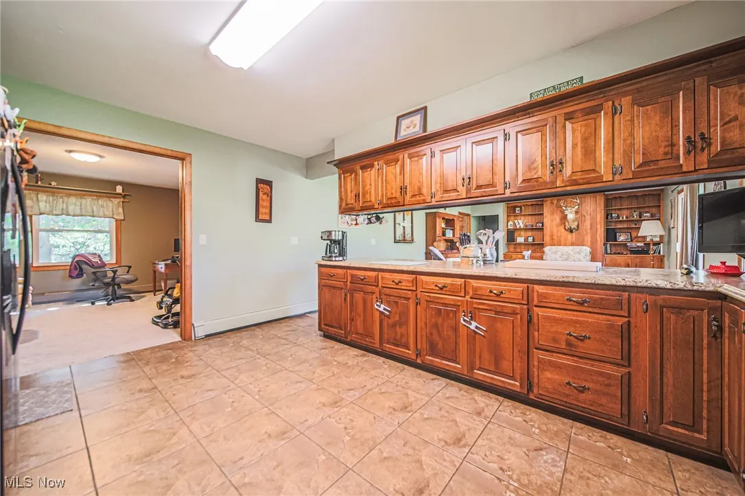 Kitchen with a baseboard heating unit, freestanding refrigerator, brown cabinets, an office area, and light tile patterned floors