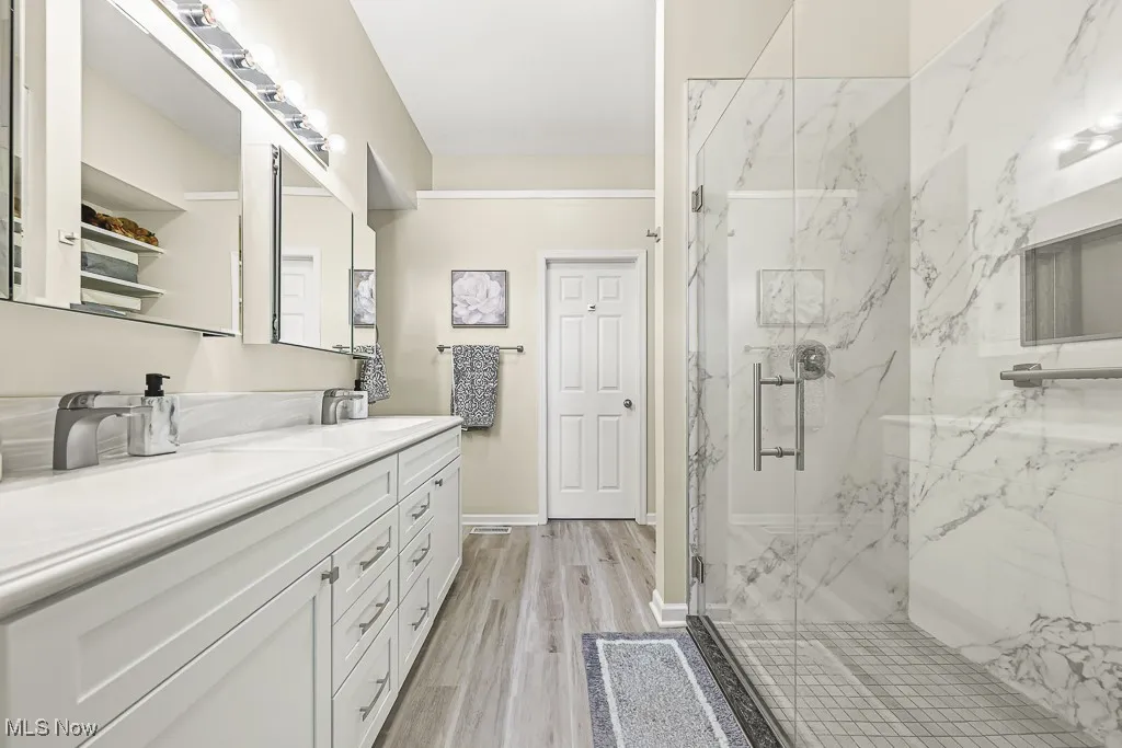Bathroom with double vanity, a marble finish shower, and light wood-type flooring
