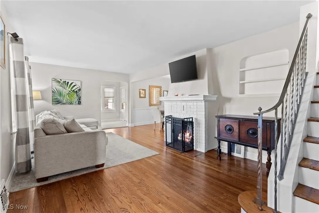 Living room with stairs, a brick fireplace, and wood finished floors