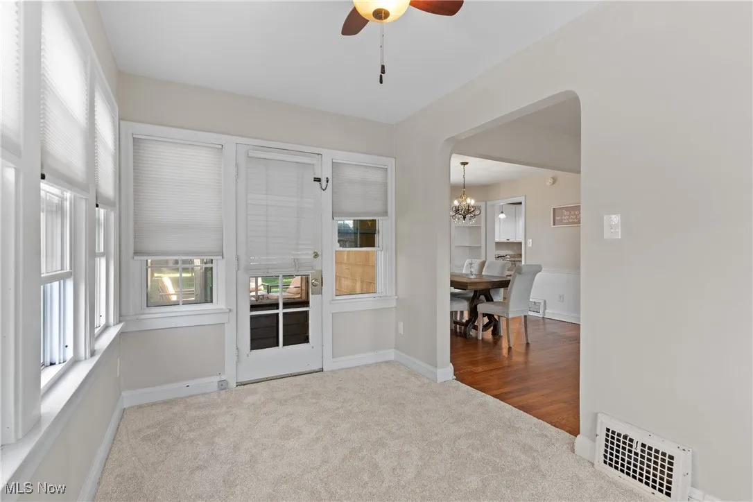 Empty room featuring light carpet, ceiling fan, a chandelier, and arched walkways