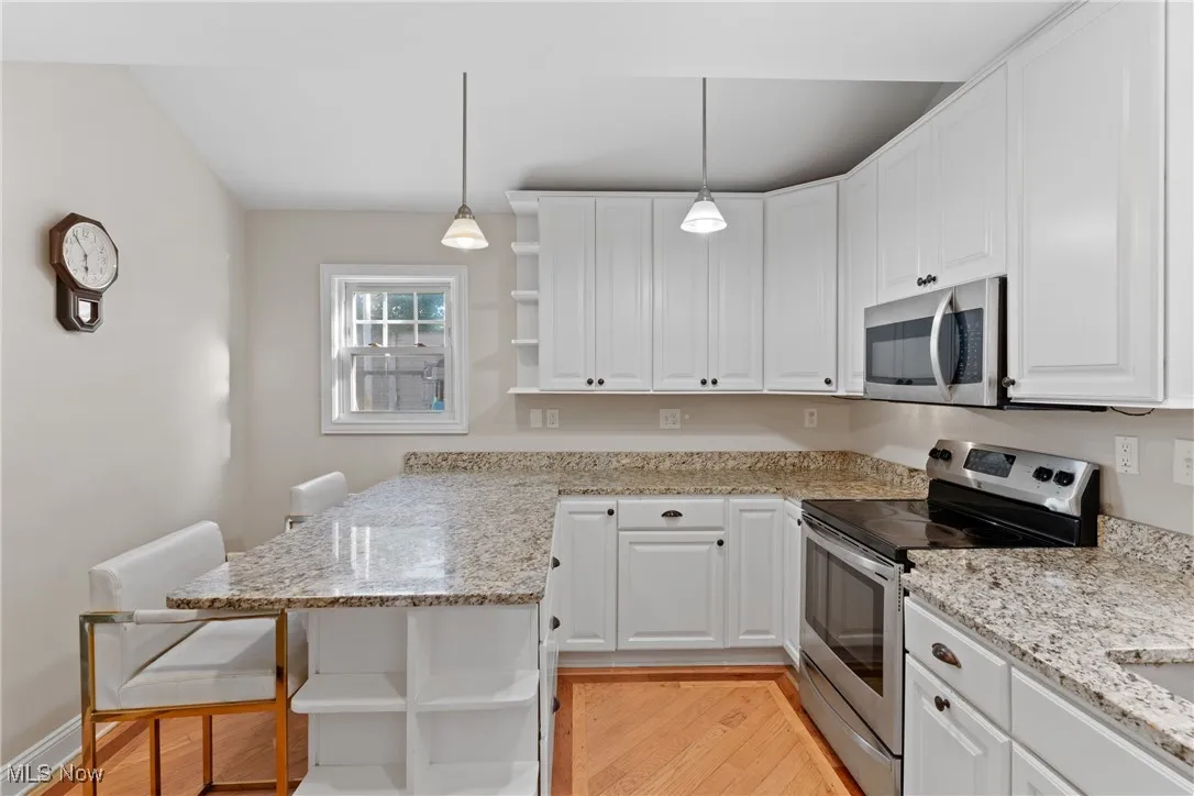 Kitchen with open shelves, appliances with stainless steel finishes, hanging light fixtures, light wood-type flooring, and a kitchen breakfast bar