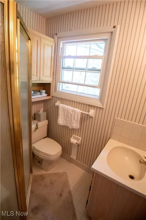 En-suite full bathroom featuring wallpapered walls, vanity, a shower stall, and light tile patterned flooring