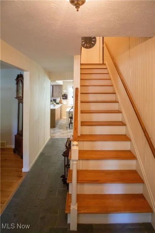 Stairs to second floor with a textured ceiling and wood finished stairs