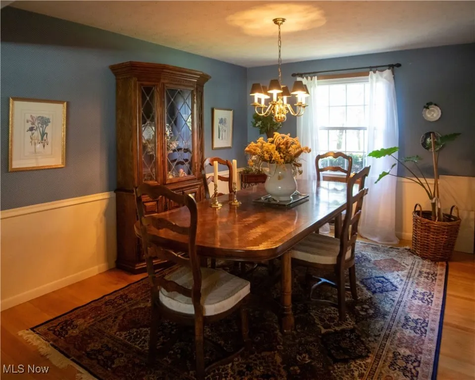 Dining room featuring light wood-type flooring, a chandelier, and wainscoting