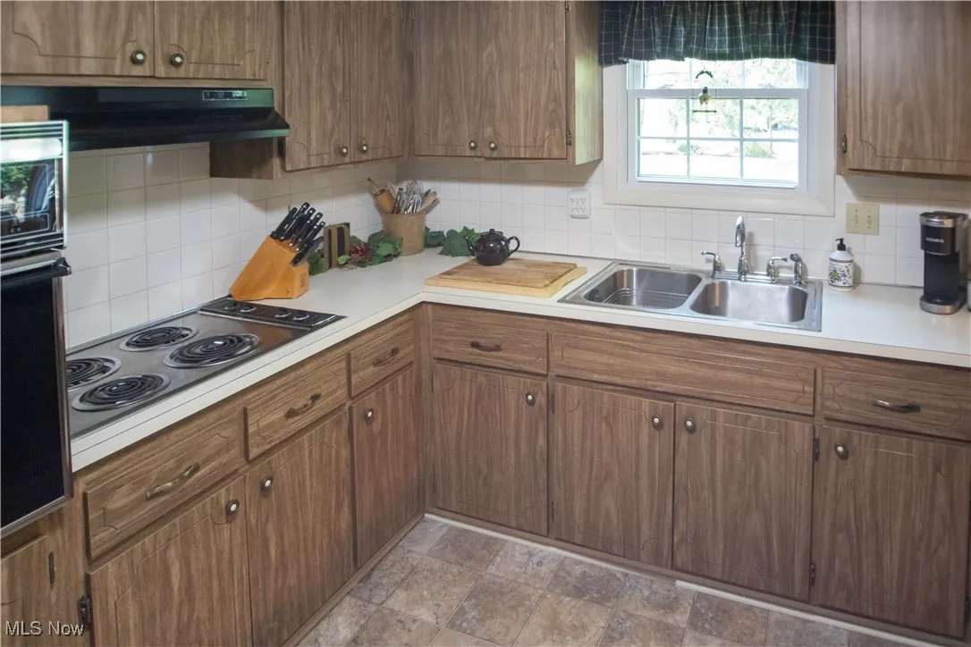 Kitchen with light countertops, decorative backsplash, oven, and stainless steel electric stovetop