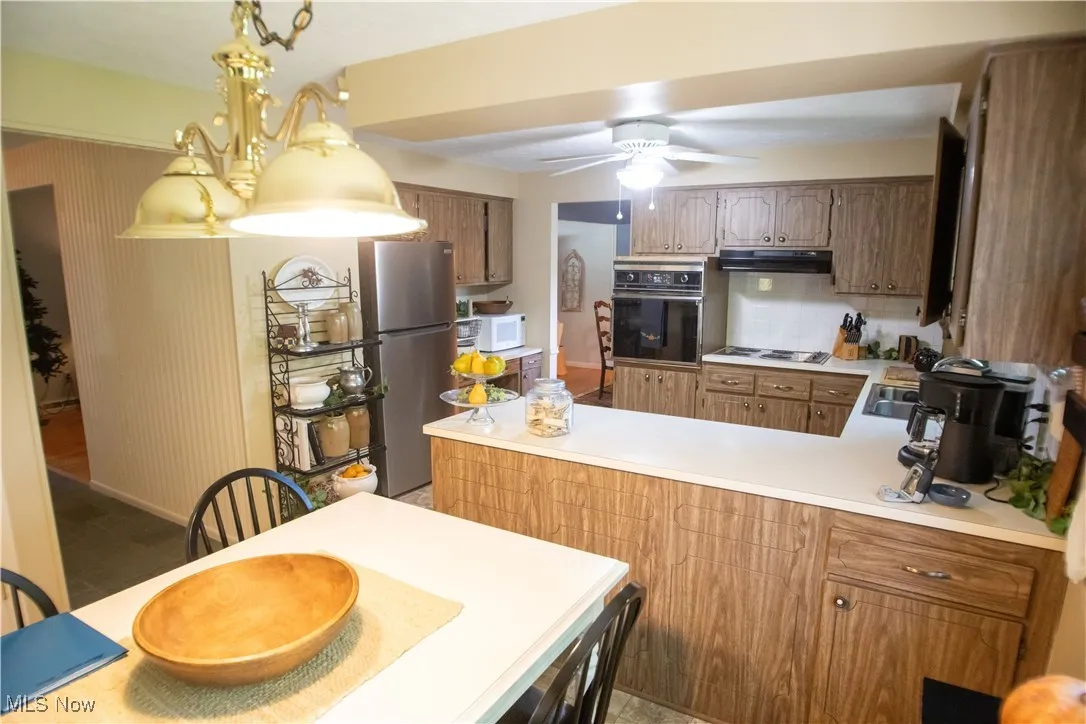 Kitchen with light countertops, black oven, freestanding refrigerator, a peninsula, and backsplash