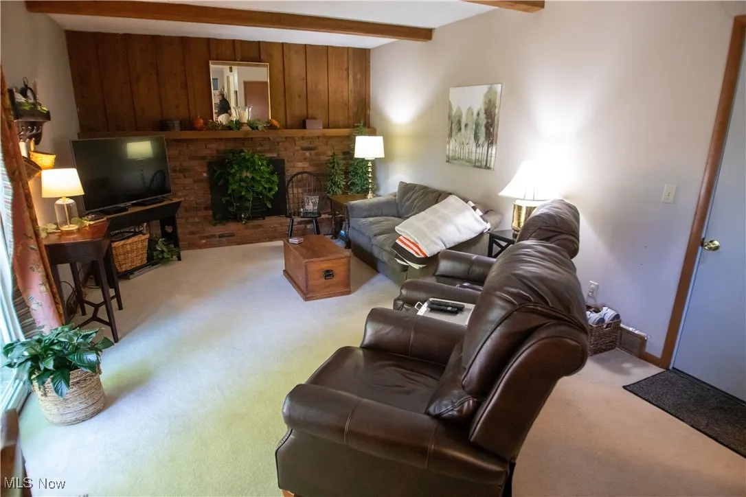 Family room featuring a brick fireplace, beam ceiling, light carpet, and wood walls