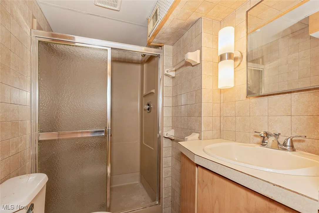 Bathroom featuring tile walls, a stall shower, and vanity