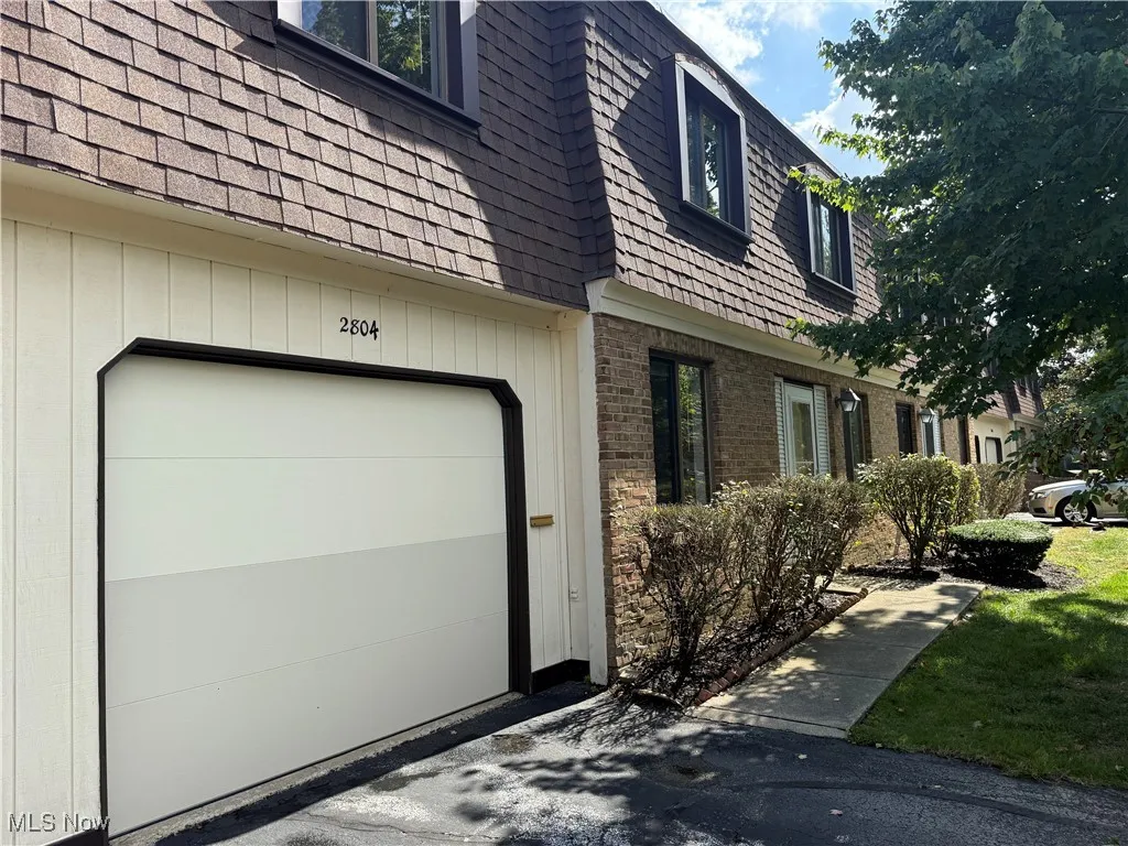 View of home's exterior with mansard roof, a garage, brick siding, and a shingled roof