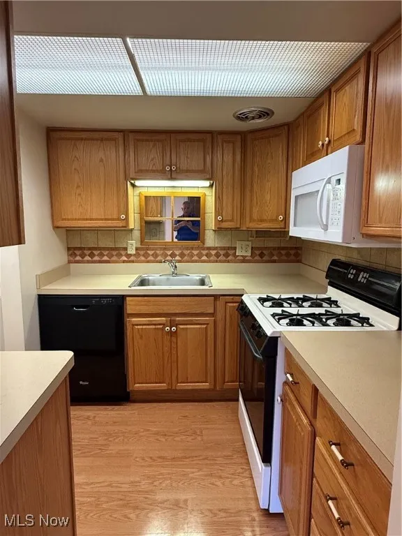 Kitchen with black appliances, brown cabinetry, decorative backsplash, and light wood-style floors