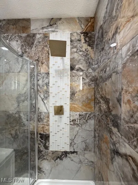Full bathroom with a marble finish shower and a textured ceiling