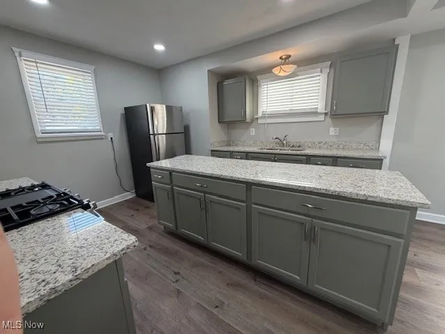 Kitchen with gray cabinets, freestanding refrigerator, a center island, light stone counters, and dark wood-type flooring