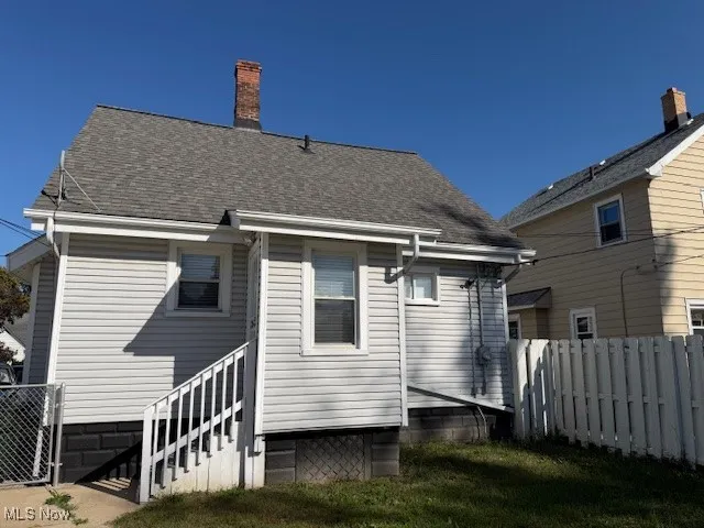 Back of property with a chimney and roof with shingles