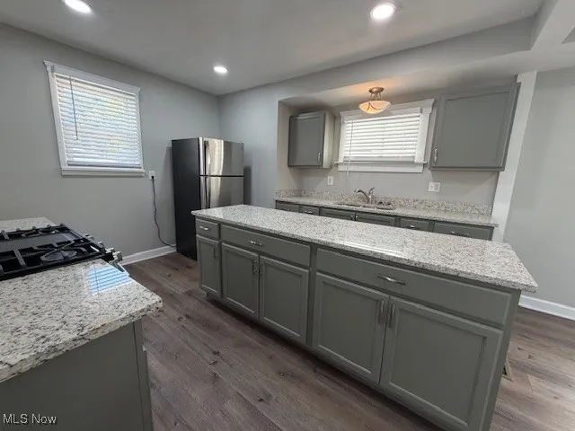 Kitchen featuring gray cabinets, dark wood-style floors, freestanding refrigerator, light stone counters, and recessed lighting