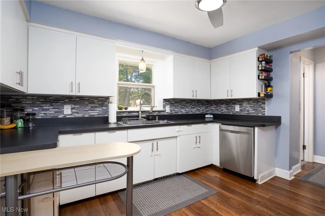 Kitchen with dark countertops, white cabinetry, dark wood-type flooring, dishwasher, and tasteful backsplash