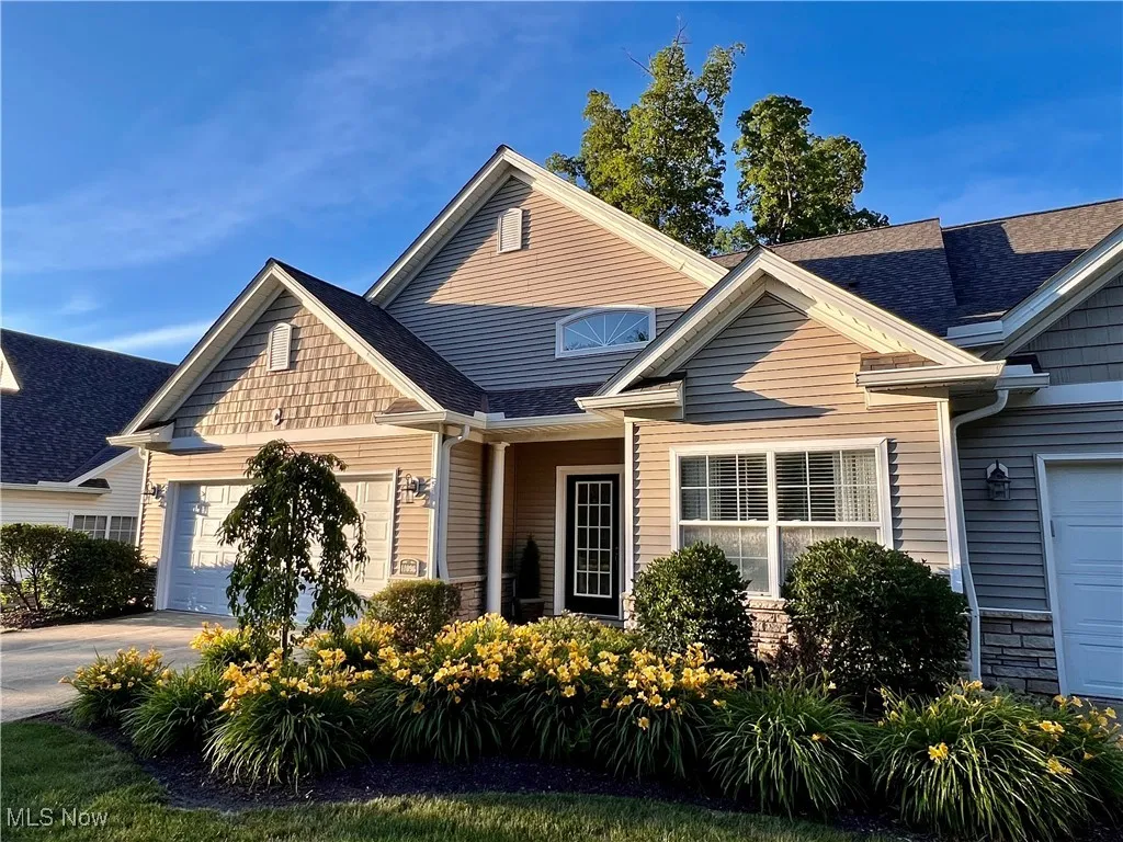 View of front of home with stone siding, roof with shingles, an attached garage, and driveway