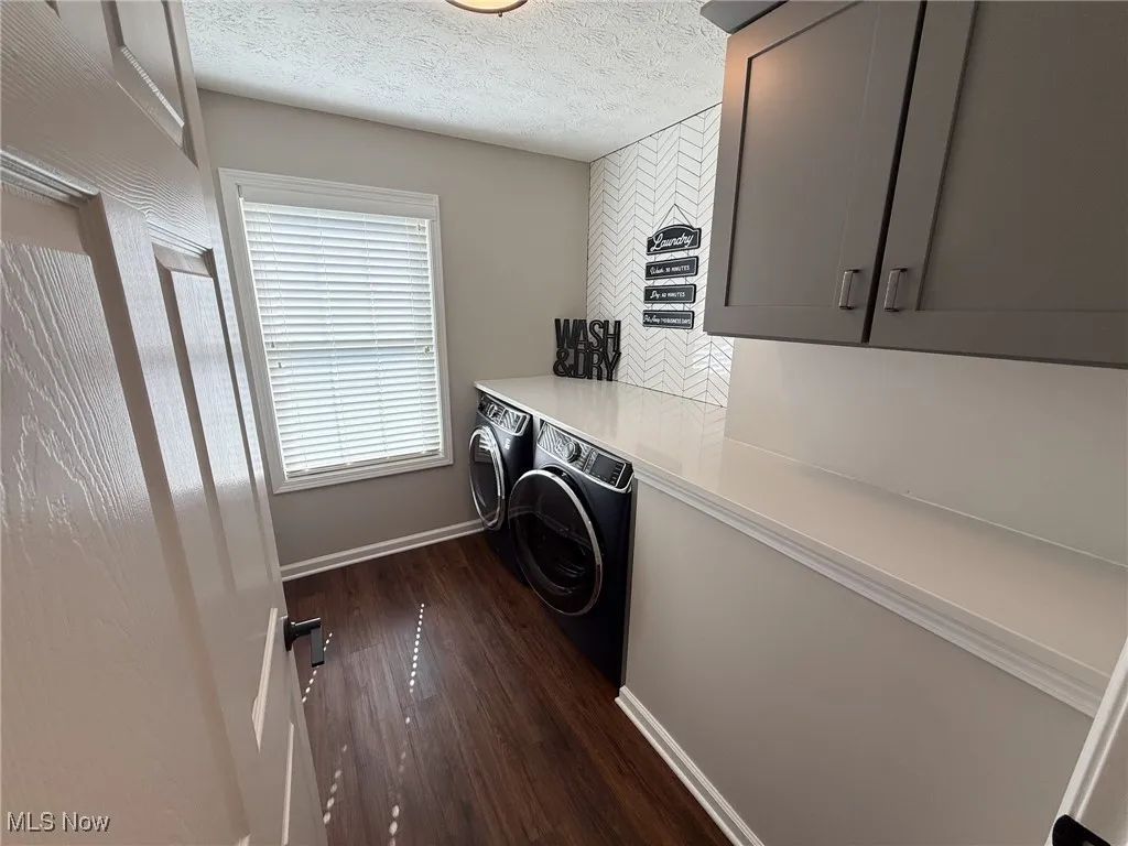 Laundry area with a textured ceiling, dark wood-type flooring, washing machine and clothes dryer, and cabinet space