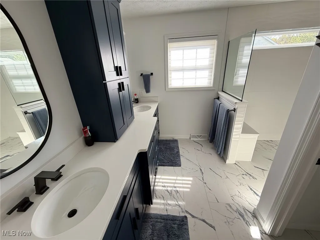 Bathroom featuring double vanity, walk in shower, light marble finish flooring, and a textured ceiling