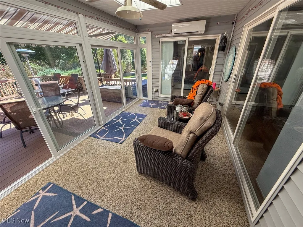 Sunroom with a skylight, a ceiling fan, carpet flooring, a wall mounted AC, and wood walls