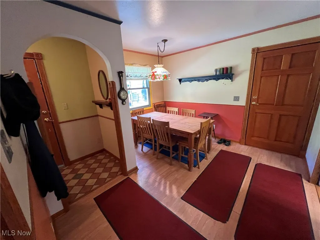 Dining space with light wood-style floors, crown molding, and arched walkways