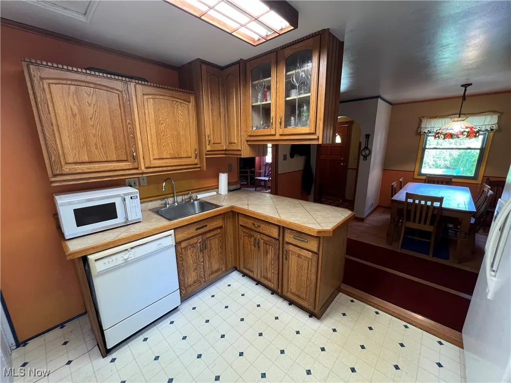 Kitchen featuring glass insert cabinets, brown cabinetry, white appliances, light floors, and ornamental molding