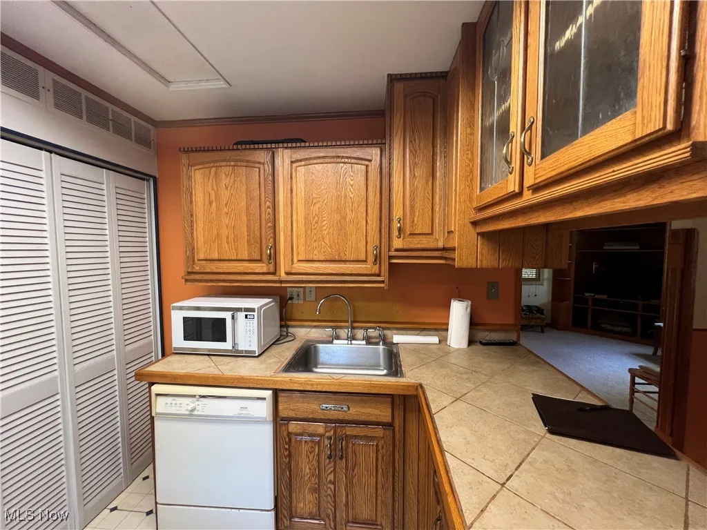 Kitchen with white appliances, glass insert cabinets, brown cabinets, and light tile patterned flooring