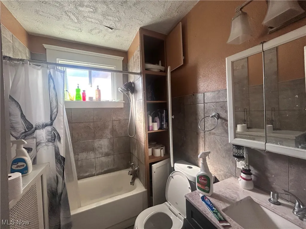 Bathroom with shower / bathtub combination with curtain, vanity, a textured ceiling, and tile walls