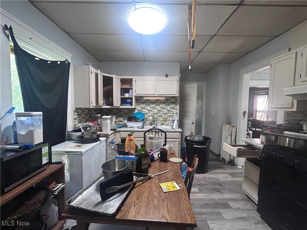 Kitchen with white cabinets, black gas range, backsplash, dark wood-style floors, and light countertops
