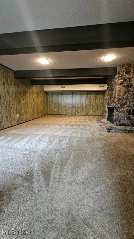 Finished below grade area featuring a textured ceiling, light colored carpet, wooden walls, and a stone fireplace