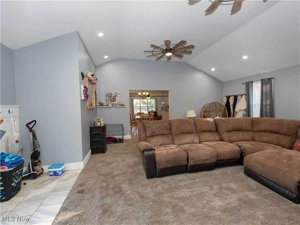 Living room featuring a ceiling fan, lofted ceiling, light carpet, recessed lighting, and a chandelier