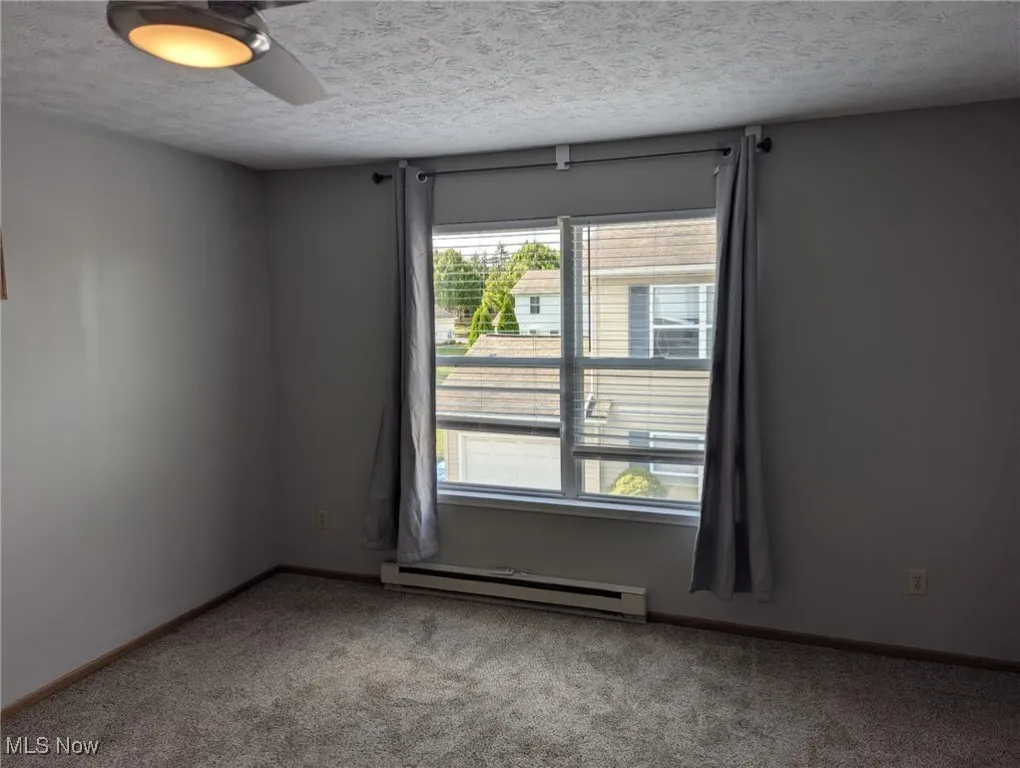 Carpeted empty room with a textured ceiling, a baseboard heating unit, and a ceiling fan