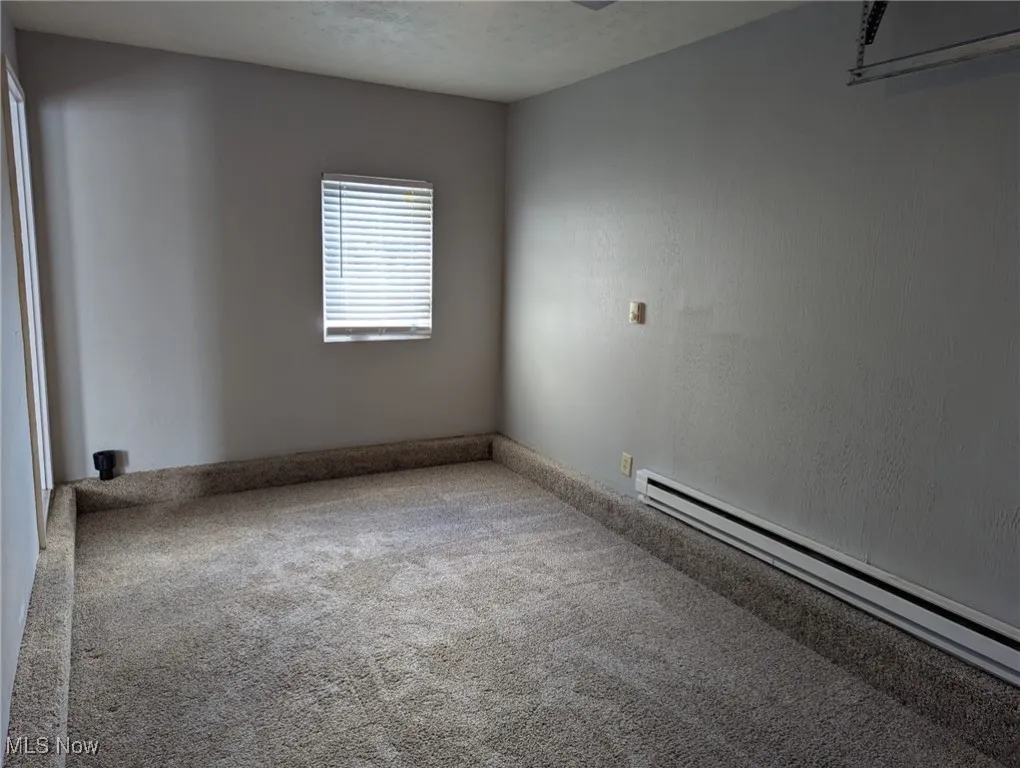 Carpeted spare room with a baseboard heating unit