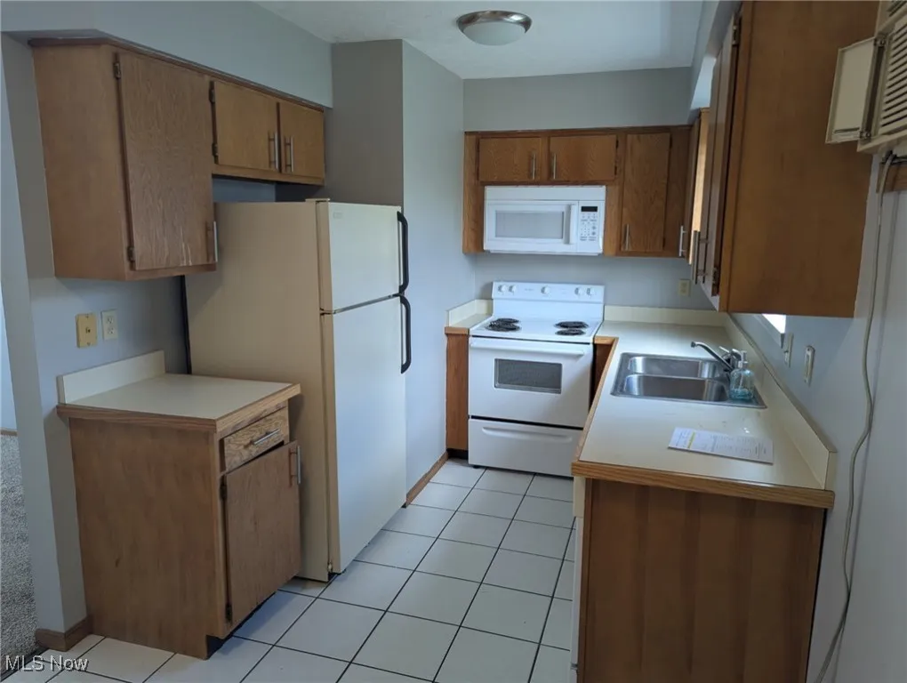 Kitchen featuring white appliances, light countertops, brown cabinetry, and light tile patterned floors
