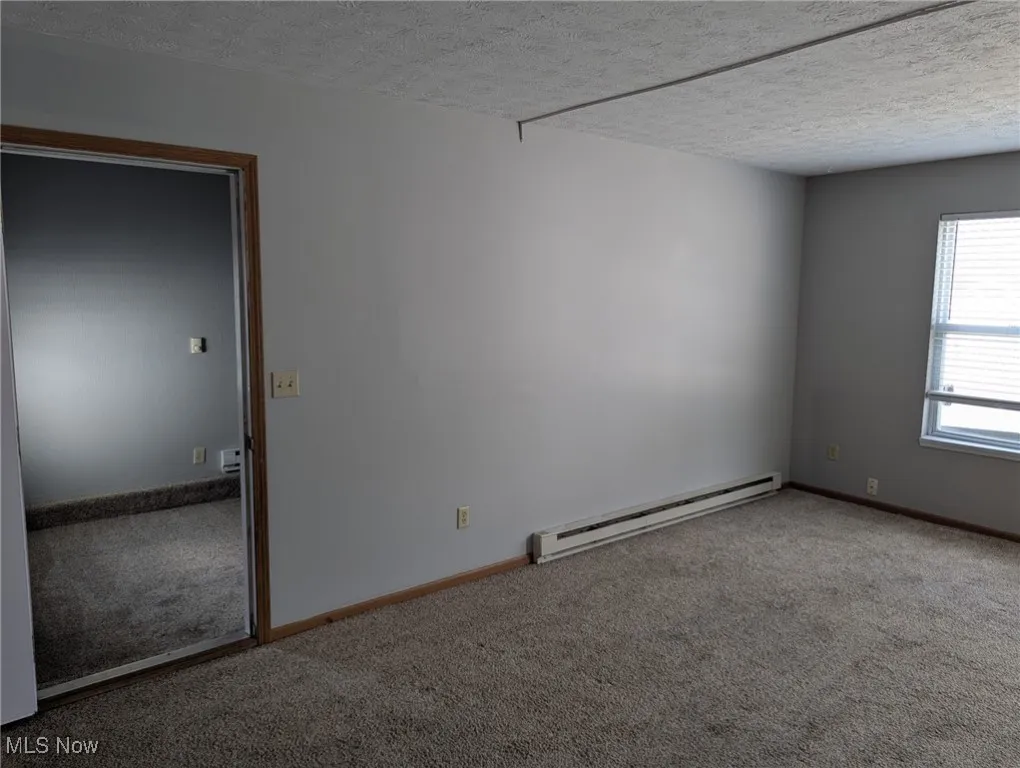 Empty room with baseboard heating, carpet, and a textured ceiling