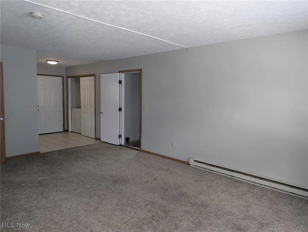 Empty room featuring a textured ceiling, light colored carpet, a baseboard radiator, and a smoke detector