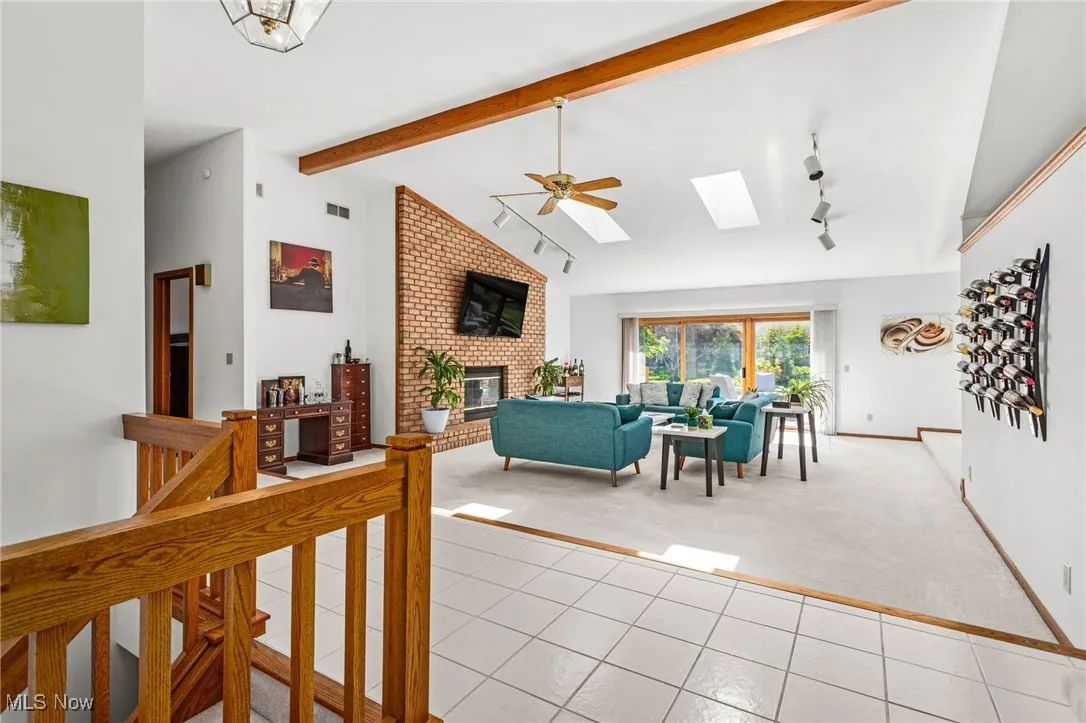 Living area with light tile patterned floors, a skylight, light carpet, a fireplace, and a ceiling fan