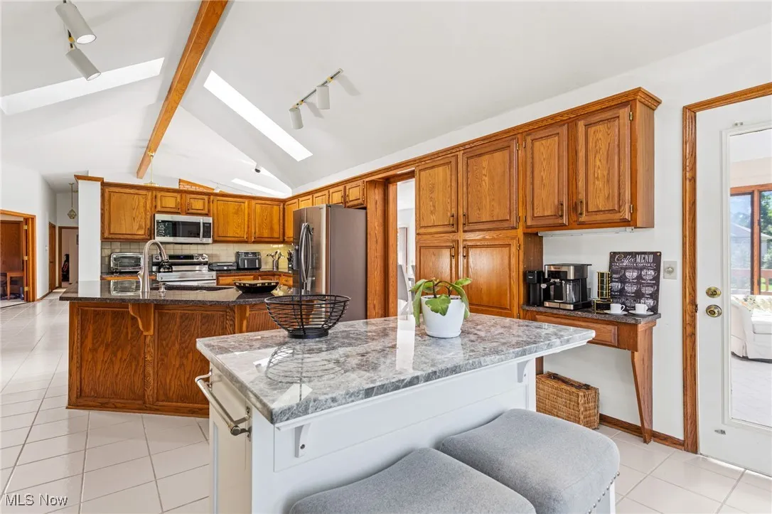 Kitchen featuring a kitchen bar, light tile patterned floors, track lighting, brown cabinetry, and a kitchen island with sink