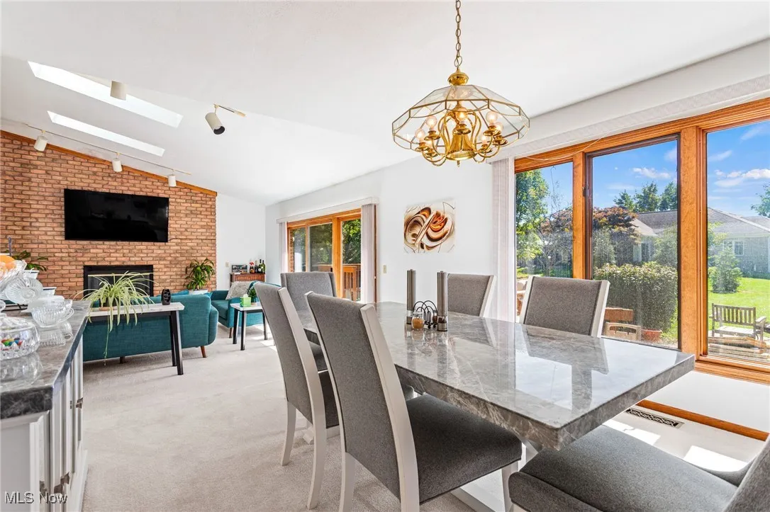 Dining space featuring a fireplace, lofted ceiling, track lighting, light carpet, and a chandelier